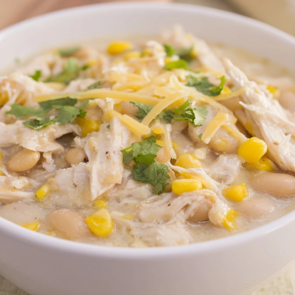 Spoon dipping into a bowl of Creamy White Chicken Chili with Corn, showing creamy texture and beans.