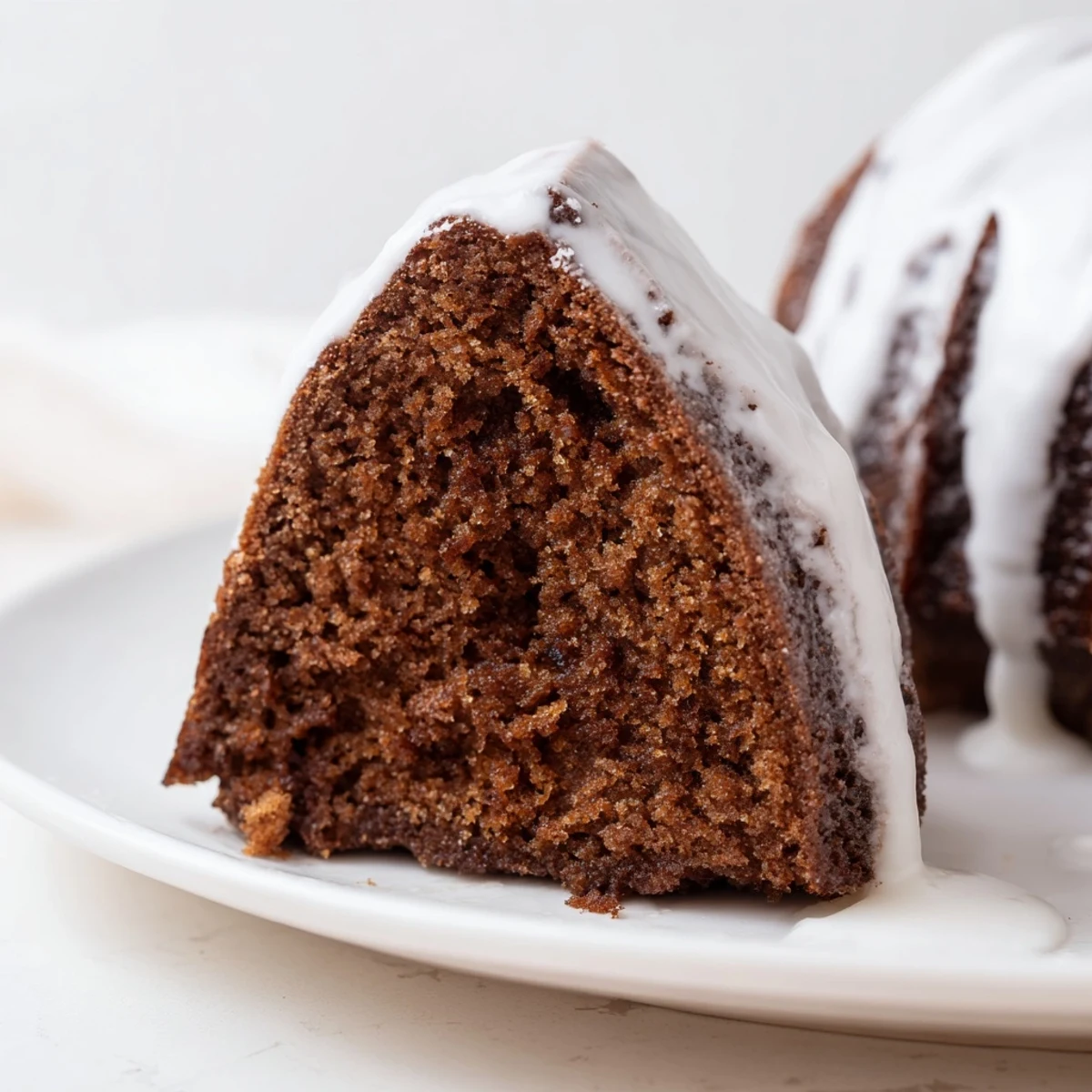 Golden Gingerbread Spiced Bundt Cake with shiny glaze, served on a white plate near festive decorations.