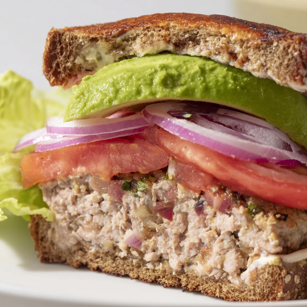 Freshly grilled turkey burger with avocado slices on a toasted whole wheat bun, garnished with tomato and lettuce.