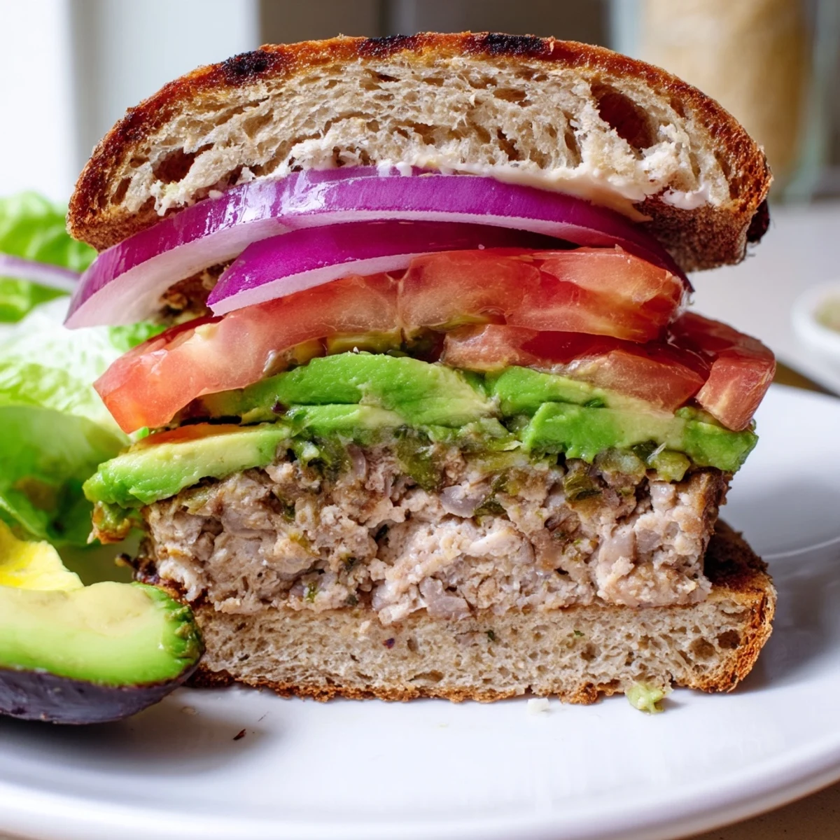 A close-up of a homemade Turkey Burger with Avocado, showing juicy patty and fresh toppings on a toasted bun.