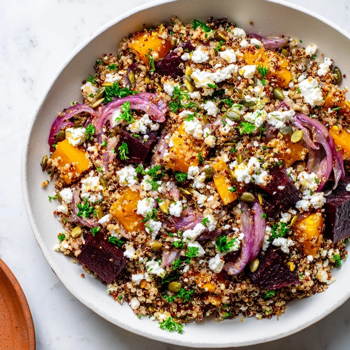 A close-up view of the finished Warm Spiced Quinoa Salad with Roasted Beets, showing glistening citrus dressing, crumbled feta, and pumpkin seeds over the warm grains and vegetables.