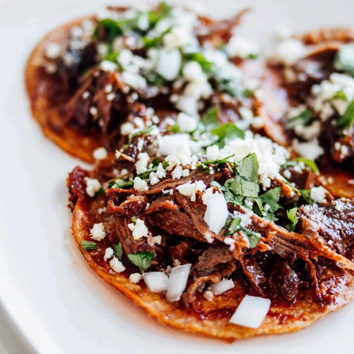 Golden-brown Slow Cooker Beef Birria Tacos with Consommé sit beside a steaming bowl of savory dipping broth.