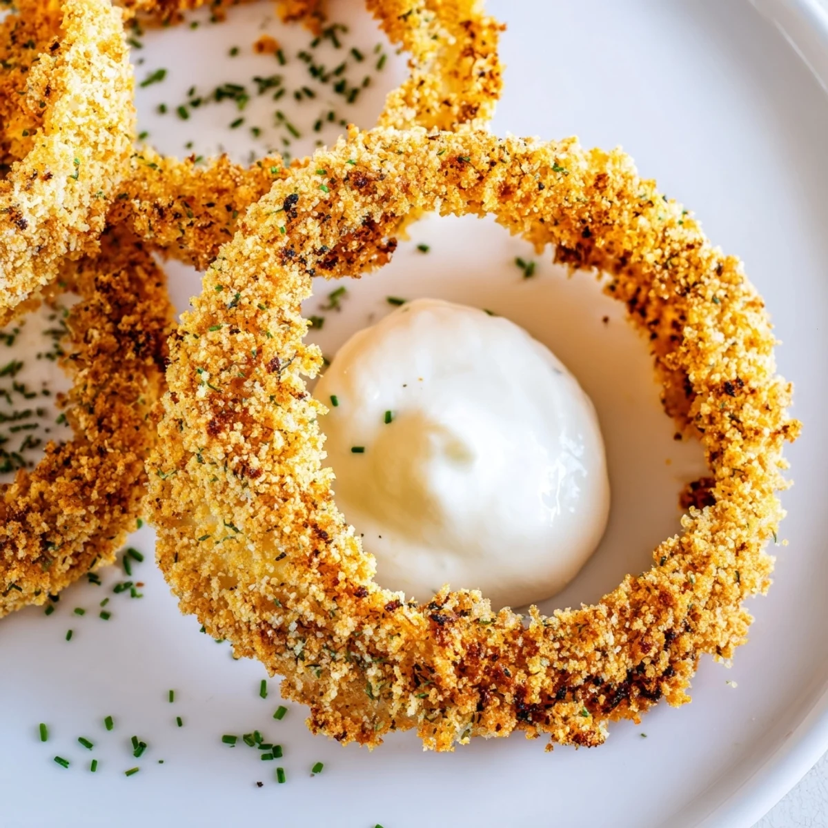 A platter of golden Crispy Baked Onion Rings with Ranch Dressing and fresh herbs.