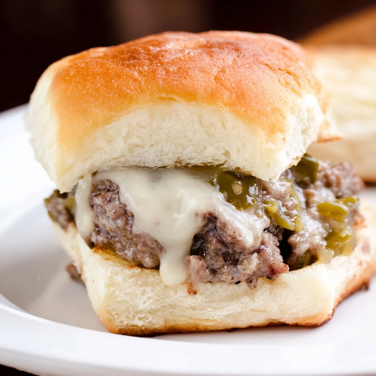 A close-up of Spicy Jalapeno Beef Sliders reveals melted pepper jack cheese and a juicy beef patty peeking from the toasted bun.  