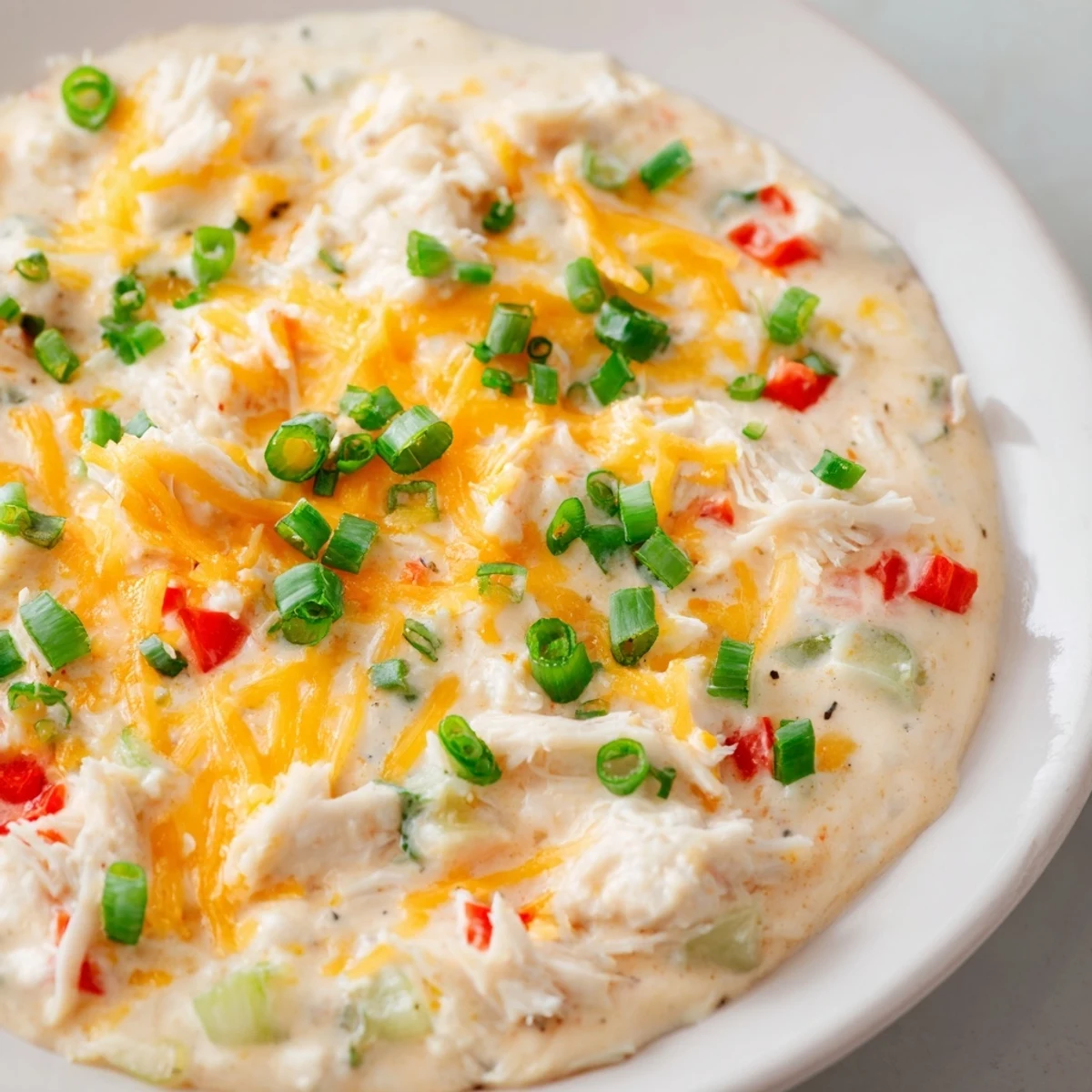 Cheesy Mardi Gras Crab Dip with red peppers and green onions in an oven-safe dish.