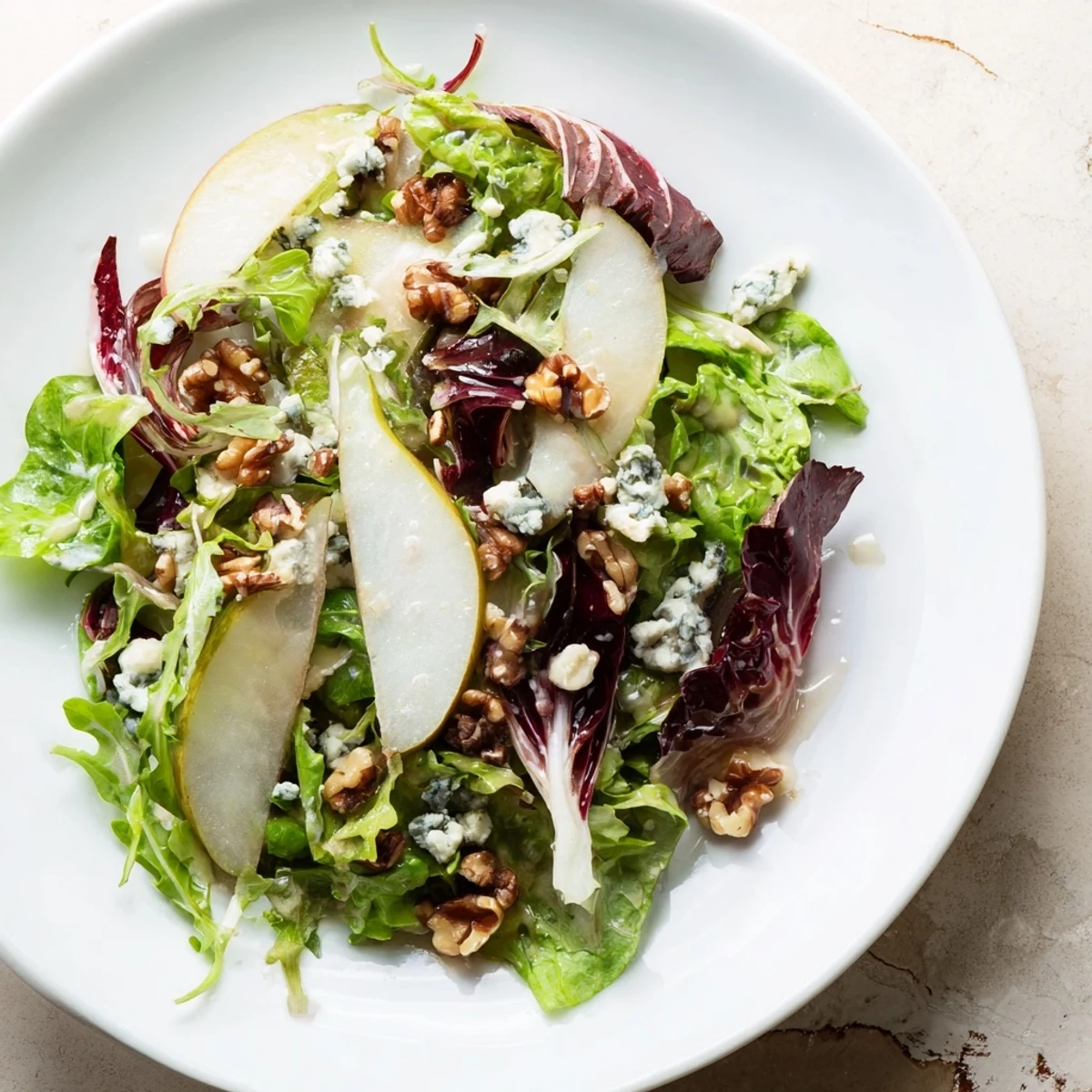 A vibrant Winter Green Salad with Pear and Walnuts tossed with tangy vinaigrette and served in a rustic ceramic bowl.  