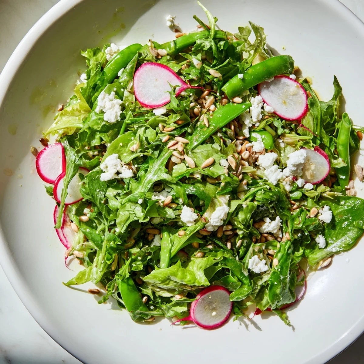 Spring greens salad with lemon vinaigrette tossed with crisp radishes and snap peas, topped with crumbled feta.
