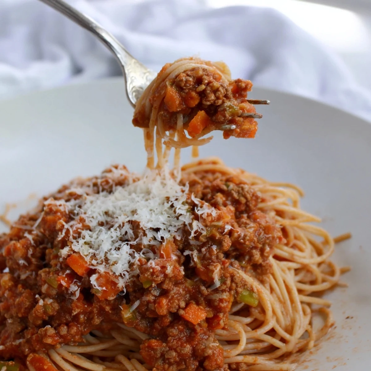 Steaming Beef Bolognese with Spaghetti and Parmesan topped with rich sauce and fresh basil in a white bowl.