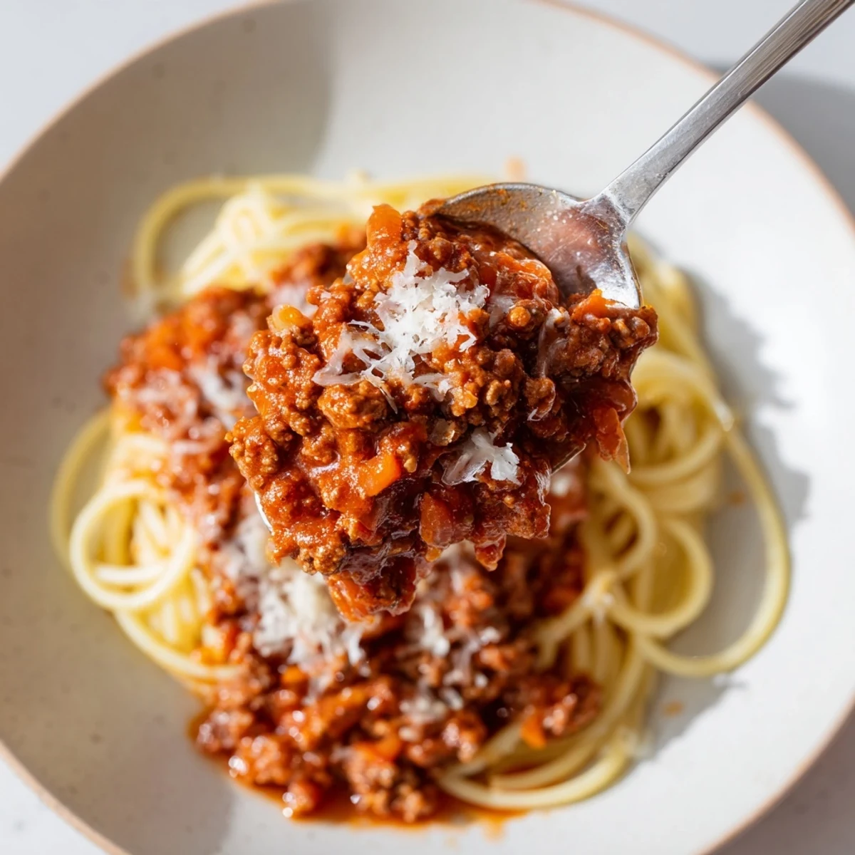 A rustic bowl of Beef Bolognese with Spaghetti and Parmesan garnished with basil leaves and melted cheese, ready to serve.