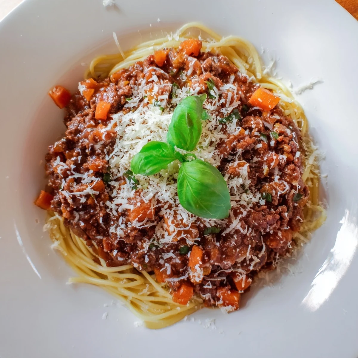 A rustic wooden table with a bowl of Beef Bolognese with Spaghetti, a glass of red wine, and crusty bread.