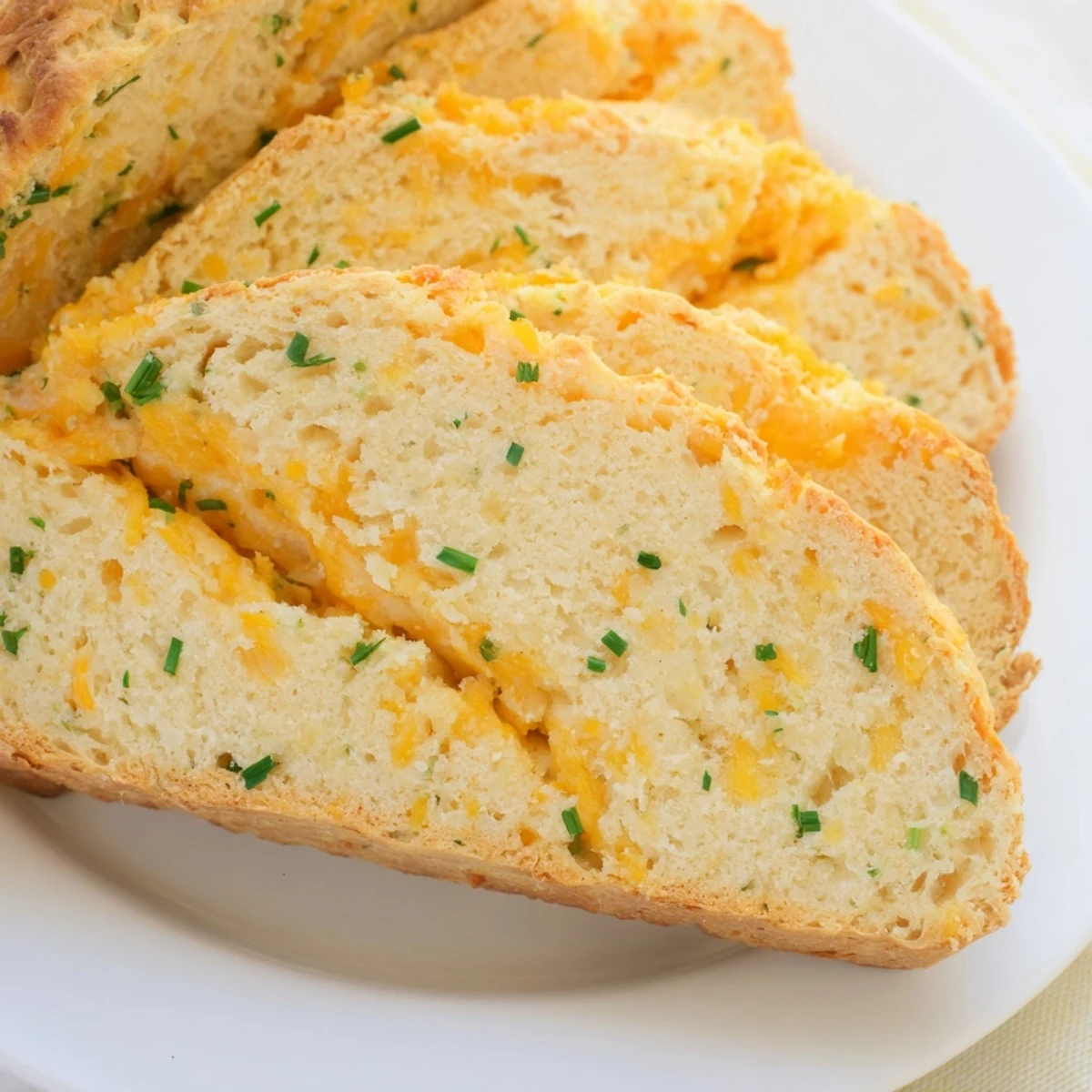 This rustic loaf of Savory Cheddar & Chive Irish Soda Bread is sliced and served with creamy butter on a cozy table.