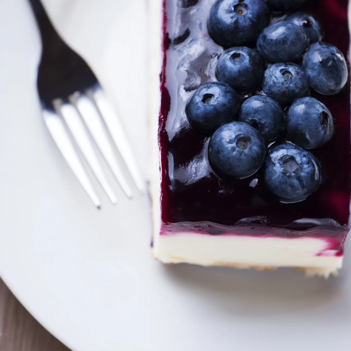 A whole Blueberry Mousse Cheesecake sits on a marble counter, ready to be sliced for a special occasion.