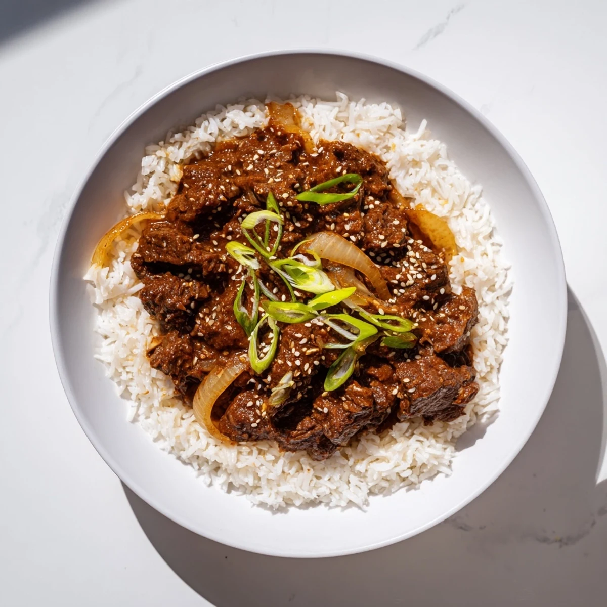 Shredded beef in a glossy Korean-inspired sauce, simmered in a crock pot and garnished with green onions and sesame seeds.