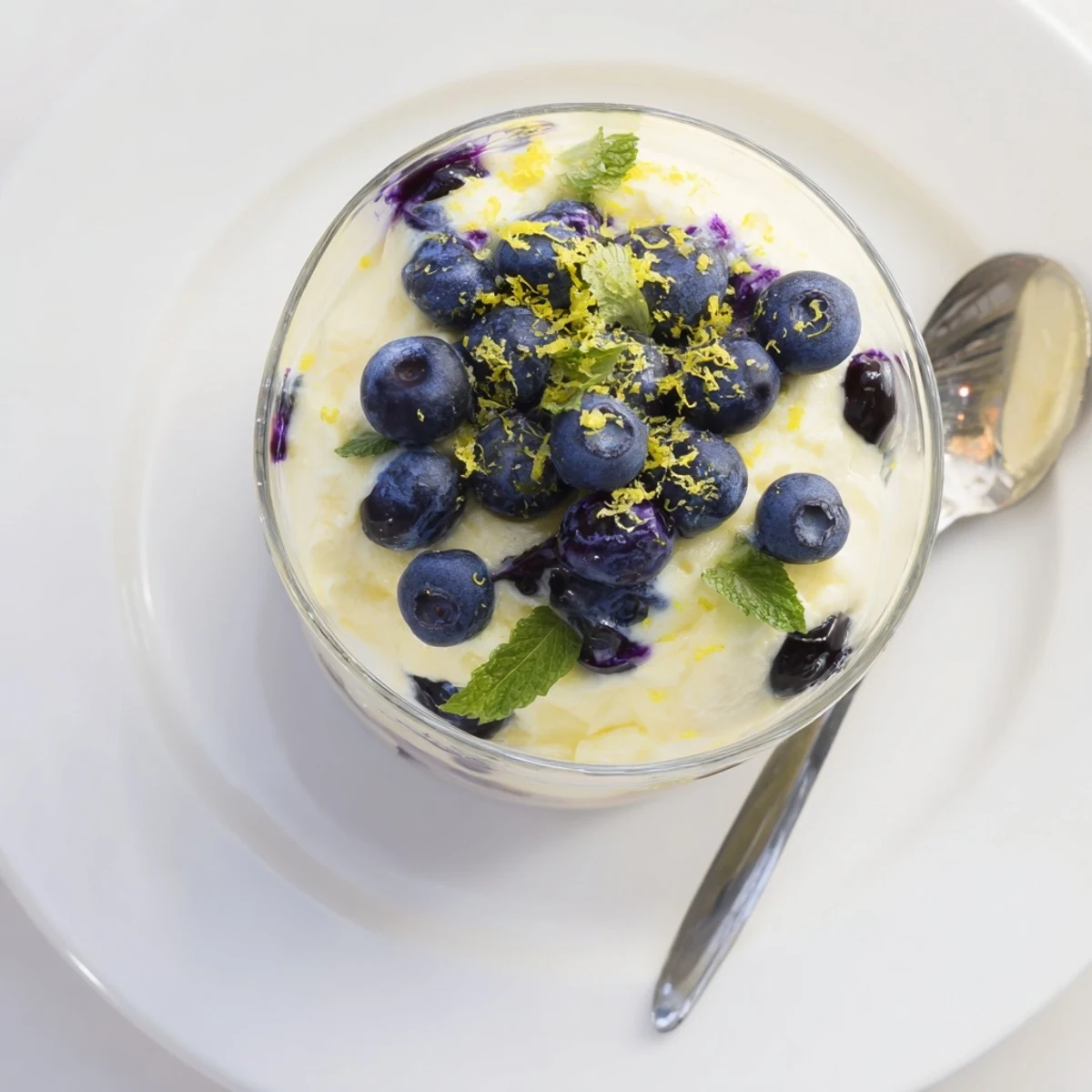 A clear glass serving dish shows layers of vibrant blueberry compote and silky Lemon Blueberry Mousse, garnished with fresh berries and lemon zest.