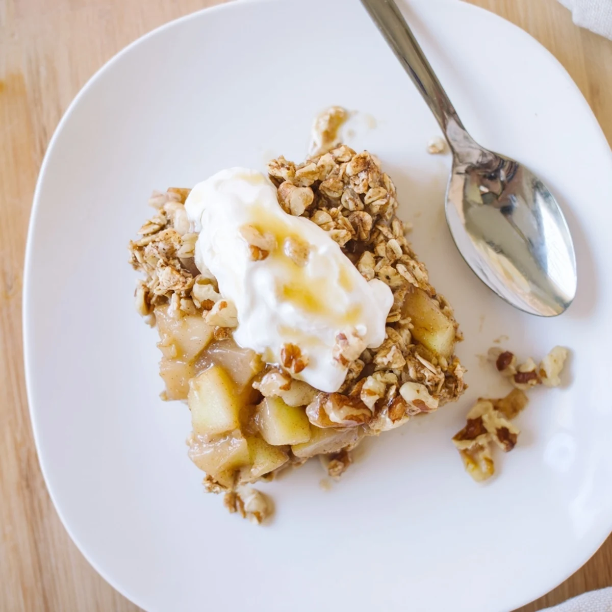 Sliced apples and walnuts top a serving of Baked Apple Oatmeal With Greek Yogurt on a rustic wooden table.