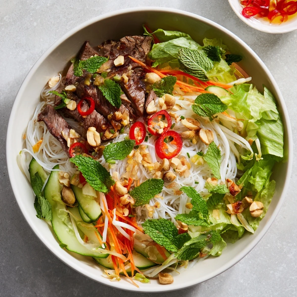 A close-up of Bun Bo Xao with sautéed beef, crisp veggies, and fresh herbs drizzled with tangy nuoc cham dressing.  