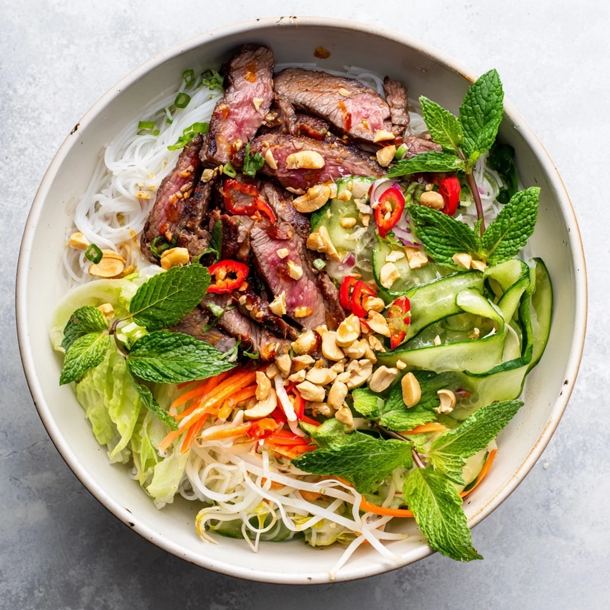 Top-down view of a colorful Bun Bo Xao bowl, vermicelli noodles topped with peanuts and fresh mint.  