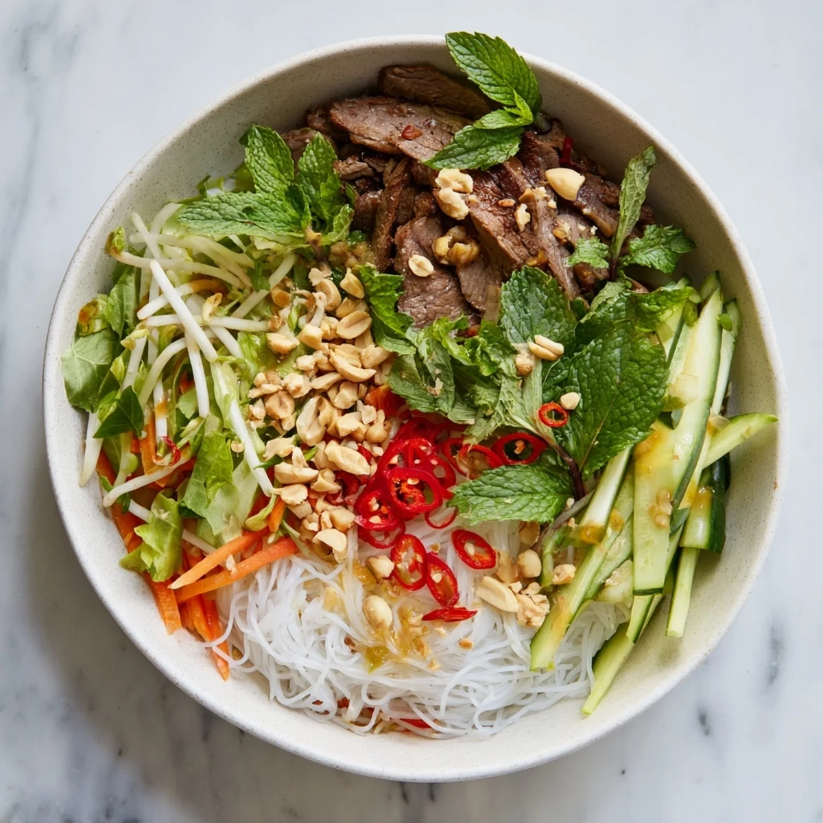 Appetizing Bun Bo Xao salad with tender beef, julienned carrots, cucumber, and lime wedges on a wooden table.