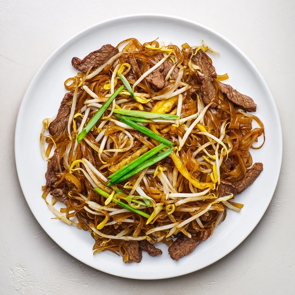 Hearty Beef Chow Fun stir-fry in a wok, glistening with savory sauce and topped with fresh scallions.