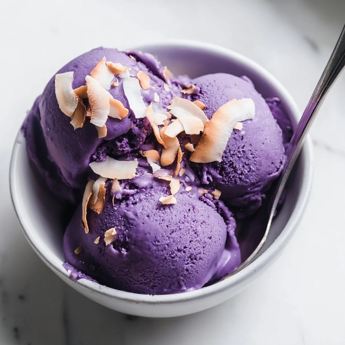 A bowl of homemade Ube Ice Cream with a vivid purple hue, scooped and topped with toasted coconut flakes for extra crunch.