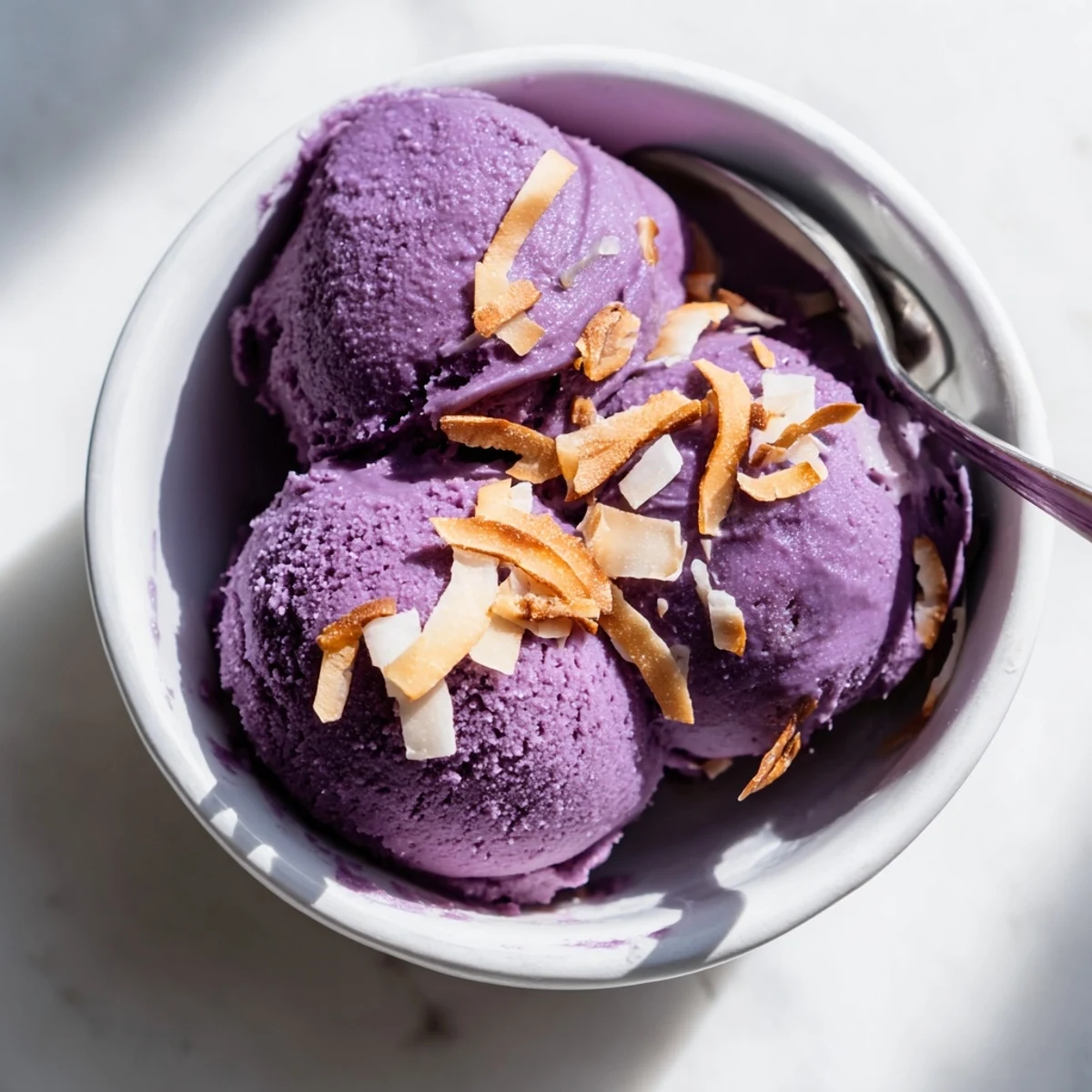 A frozen scoop of vibrant Ube Ice Cream on a cone, served against a pastel background to highlight its beautiful purple color.