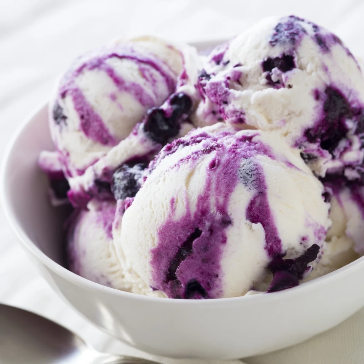 Two chilled bowls of high-protein Blueberry Cottage Cheese Ice Cream topped with a sprinkle of granola and ripe blueberries.