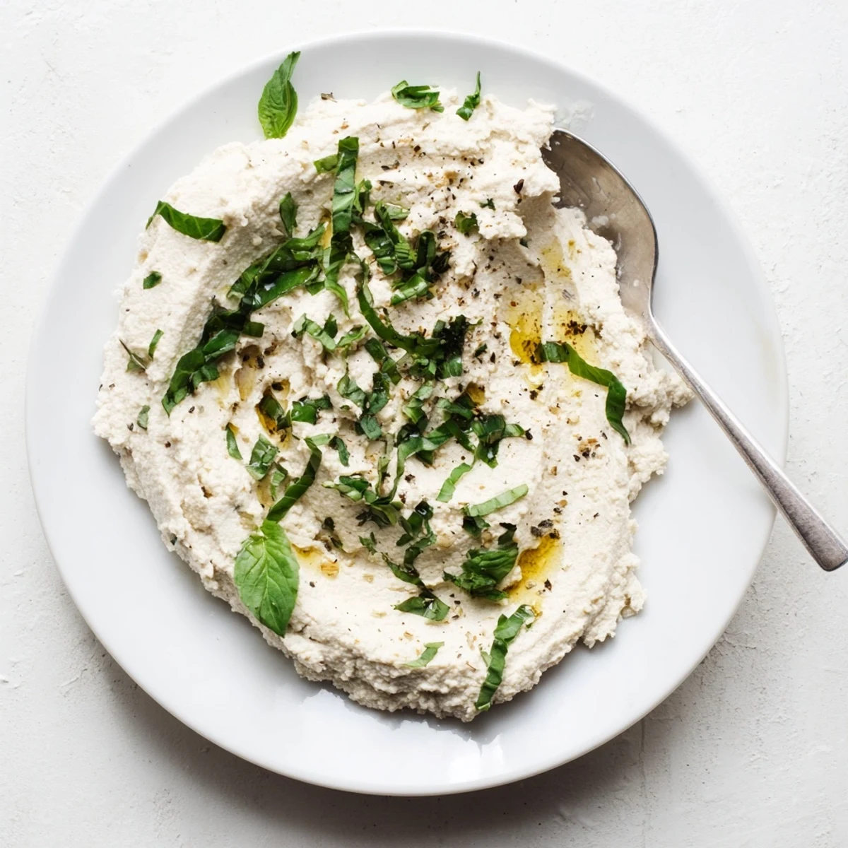 Creamy vegan Tofu Ricotta being spread on a lasagna noodle in a bright kitchen.