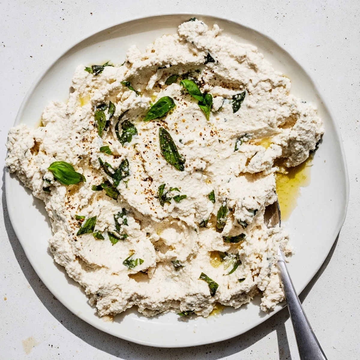A close-up of homemade Tofu Ricotta in a white bowl next to fresh basil.