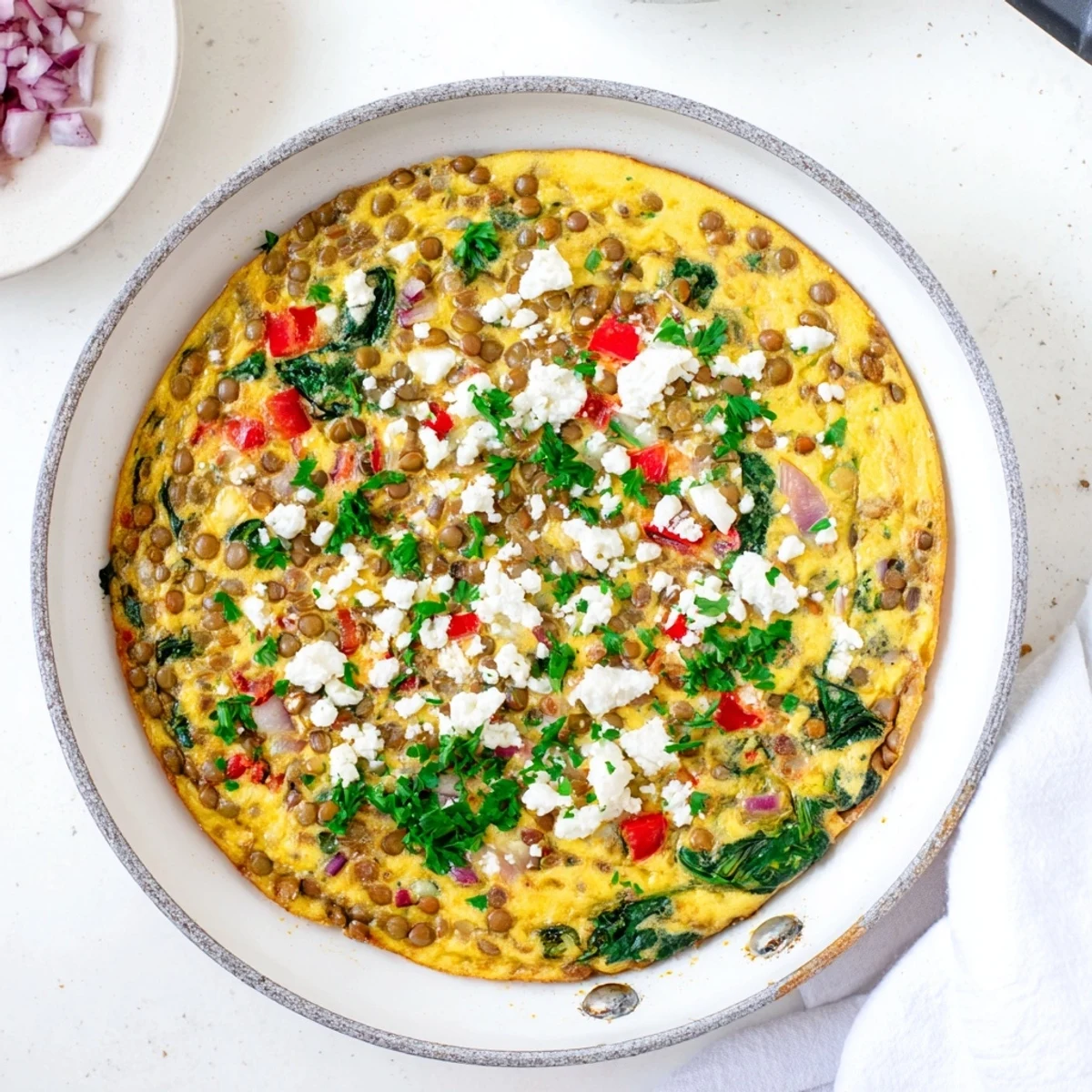 Golden slices of Healthy Lentil and Frittata rest on a white plate, showcasing chunks of creamy feta and wilted spinach.