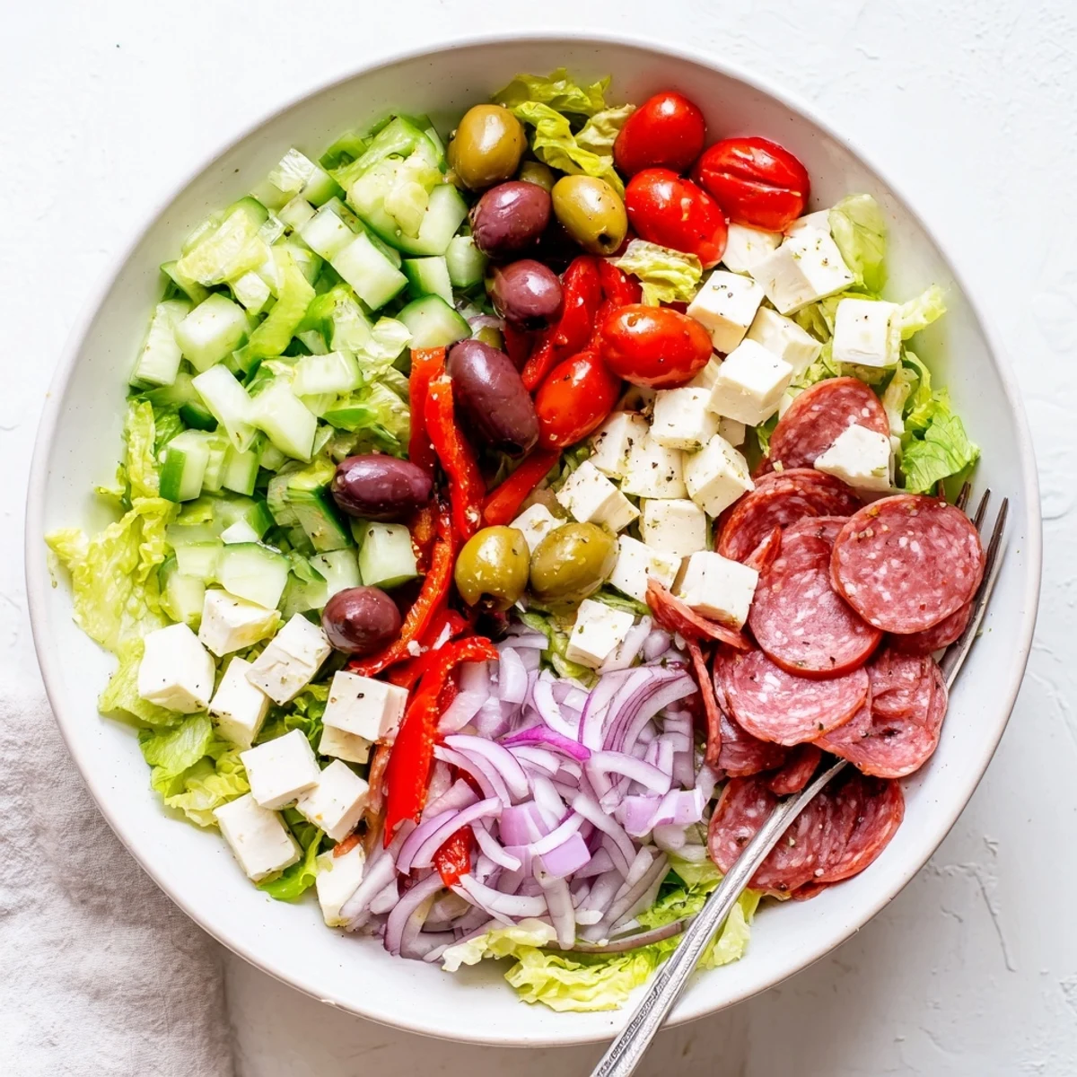 Colorful bowl of Italian chopped salad featuring romaine, tomatoes, olives, and creamy cheese cubes