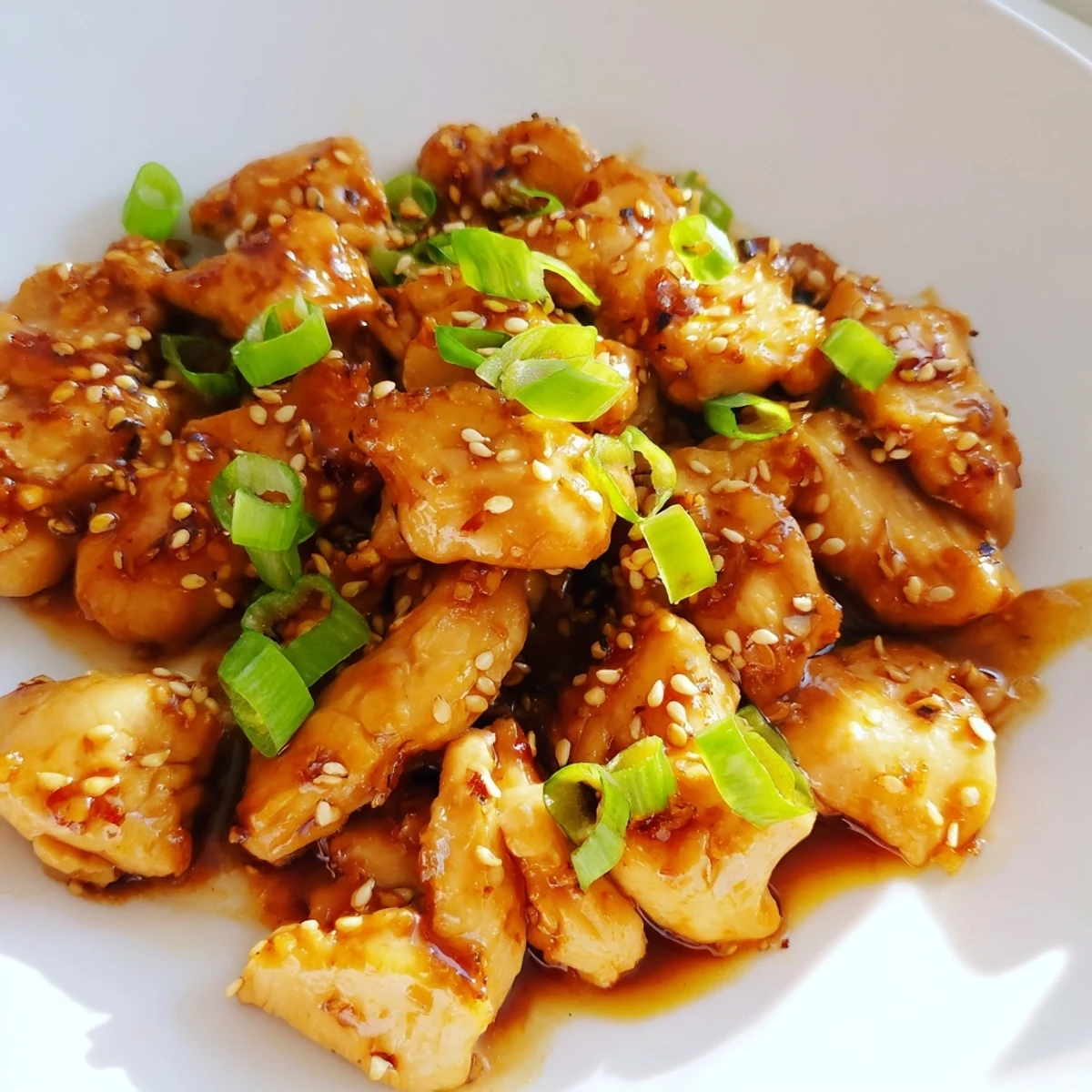 Garnished slow cooker Mongolian chicken displaying tender meat in thickened hoisin-honey glaze with fresh green onion strips.