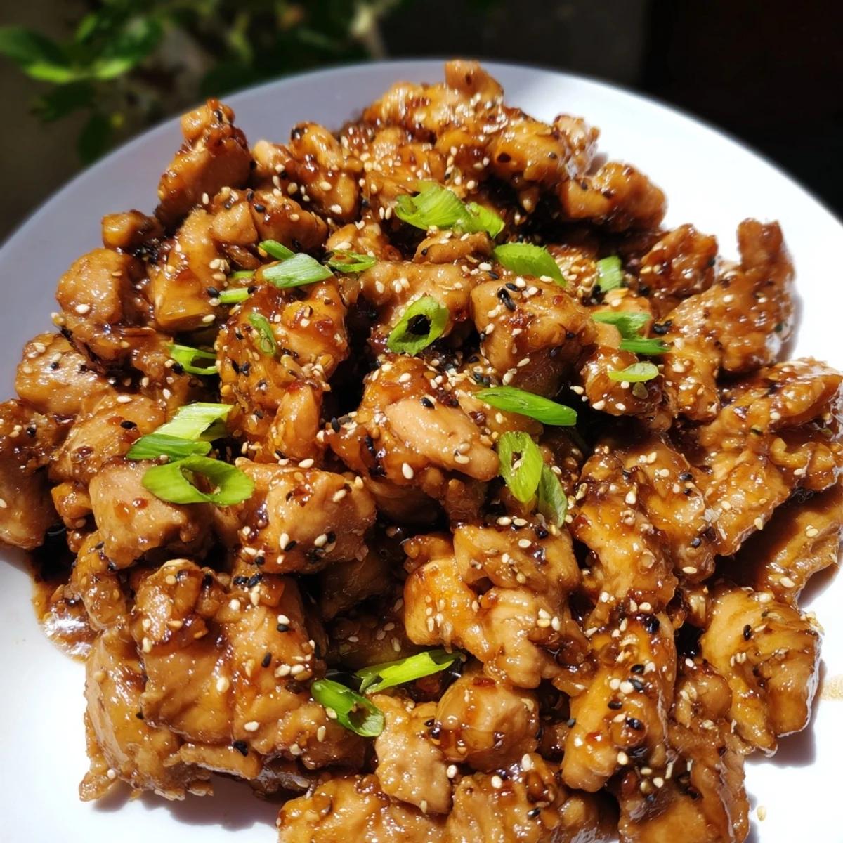 Plate of slow cooker Mongolian chicken showcasing shredded chicken thighs in savory-sweet brown sauce topped with sesame seeds.