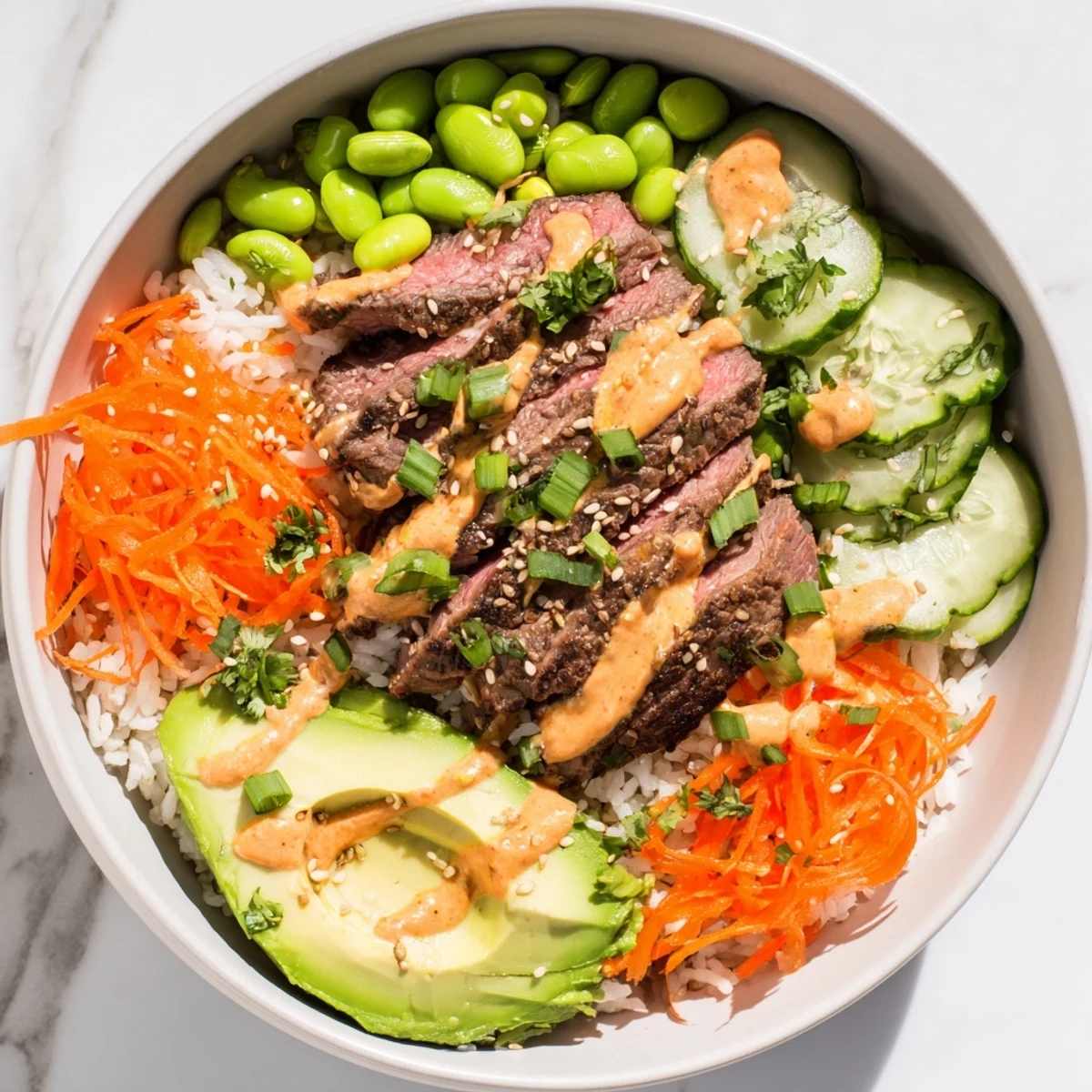 Sliced marinated flank steak bowl over rice with fresh vegetables and spicy sriracha drizzle