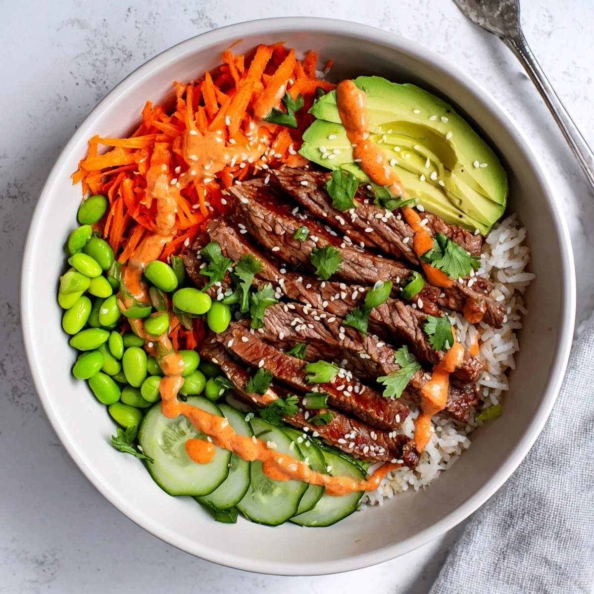 Protein-packed flank steak bowl featuring colorful carrots, cucumber, avocado, and creamy zesty sauce
