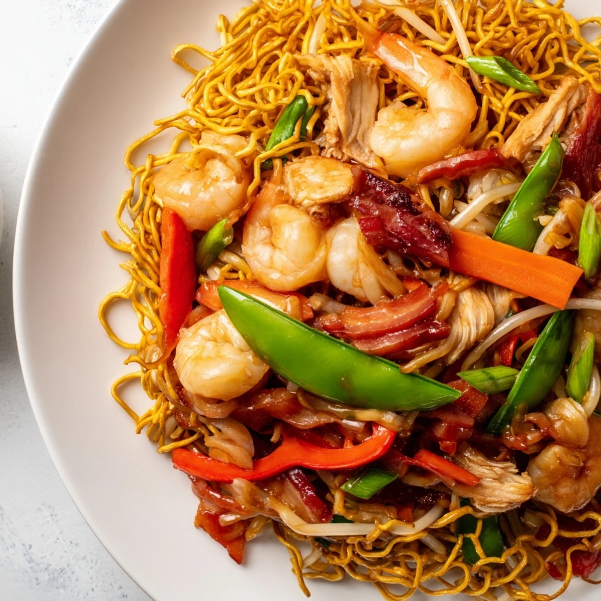 Steaming plate of Cantonese chow mein featuring crispy noodles with protein and vegetable medley