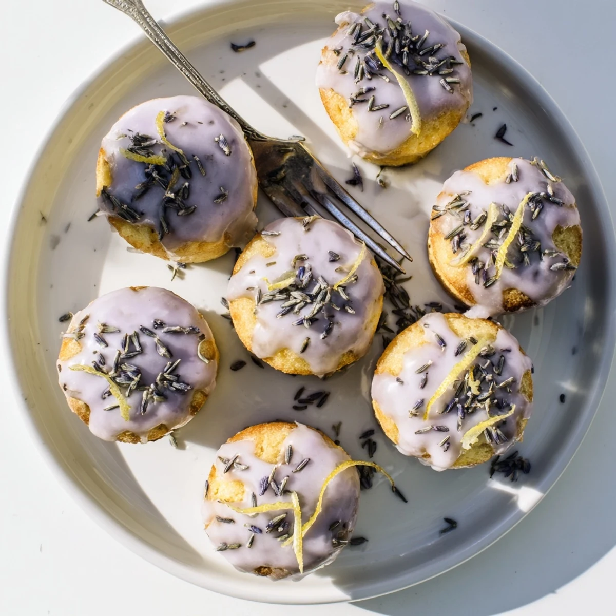 Golden mini lemon cakes with lavender glaze drizzled over tops on white plate