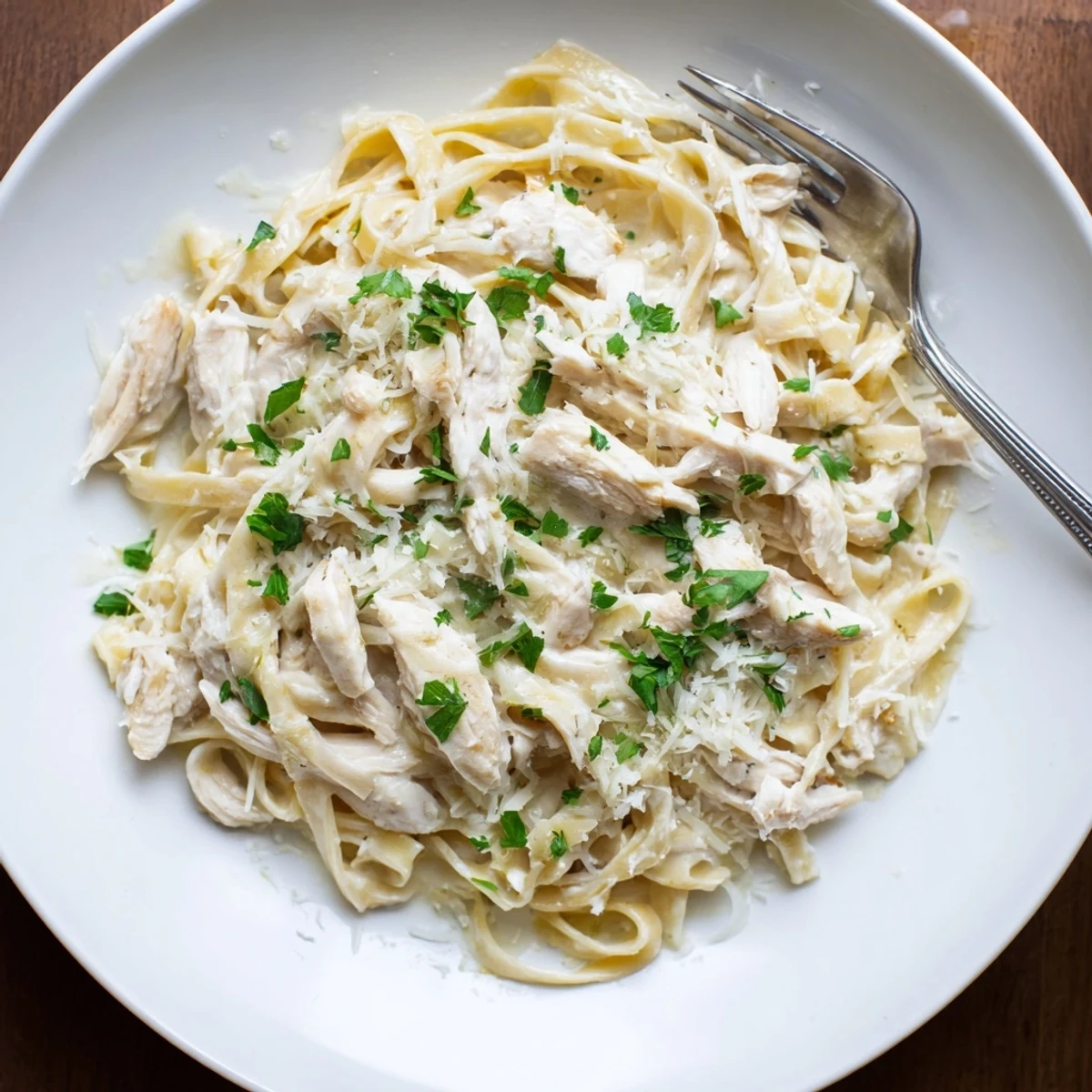 Slow cooker Chicken Alfredo featuring fettuccine coated in garlic Parmesan cream sauce with parsley.