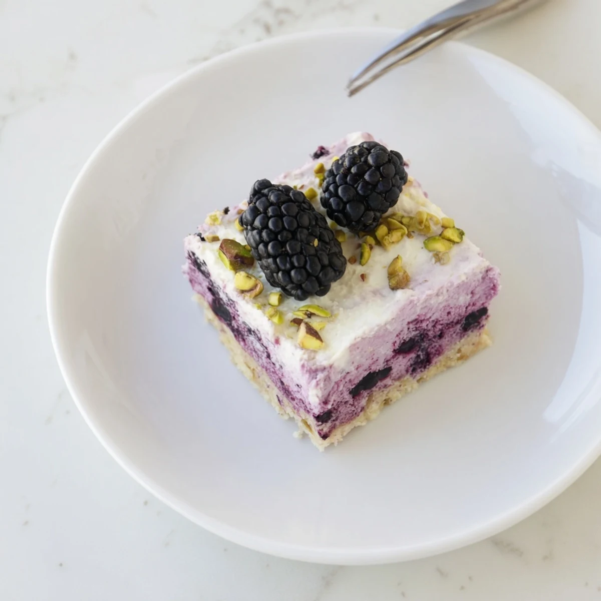 Golden square slices of Blackberry Pistachio Dream Bars layered with vibrant purple berry compote and creamy white cheesecake topping, garnished with green chopped nuts