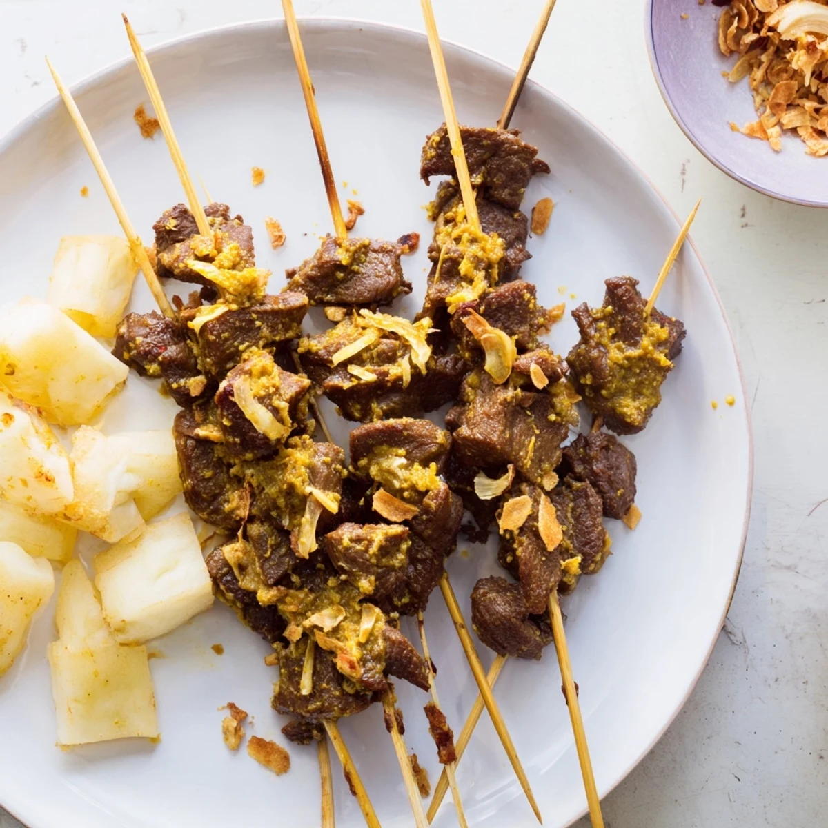 Savory Padang-style beef satay with creamy turmeric-spiced dipping sauce beside sliced rice cake and fresh herb garnish
