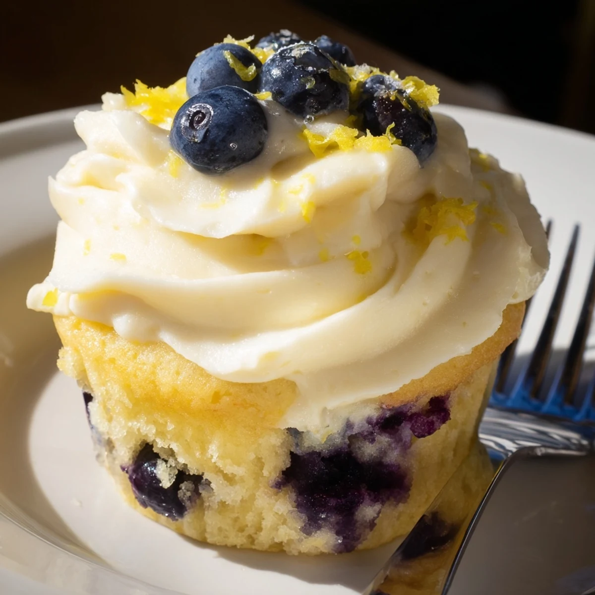 Fresh lemon blueberry cupcakes topped with tangy cream cheese frosting on a white plate