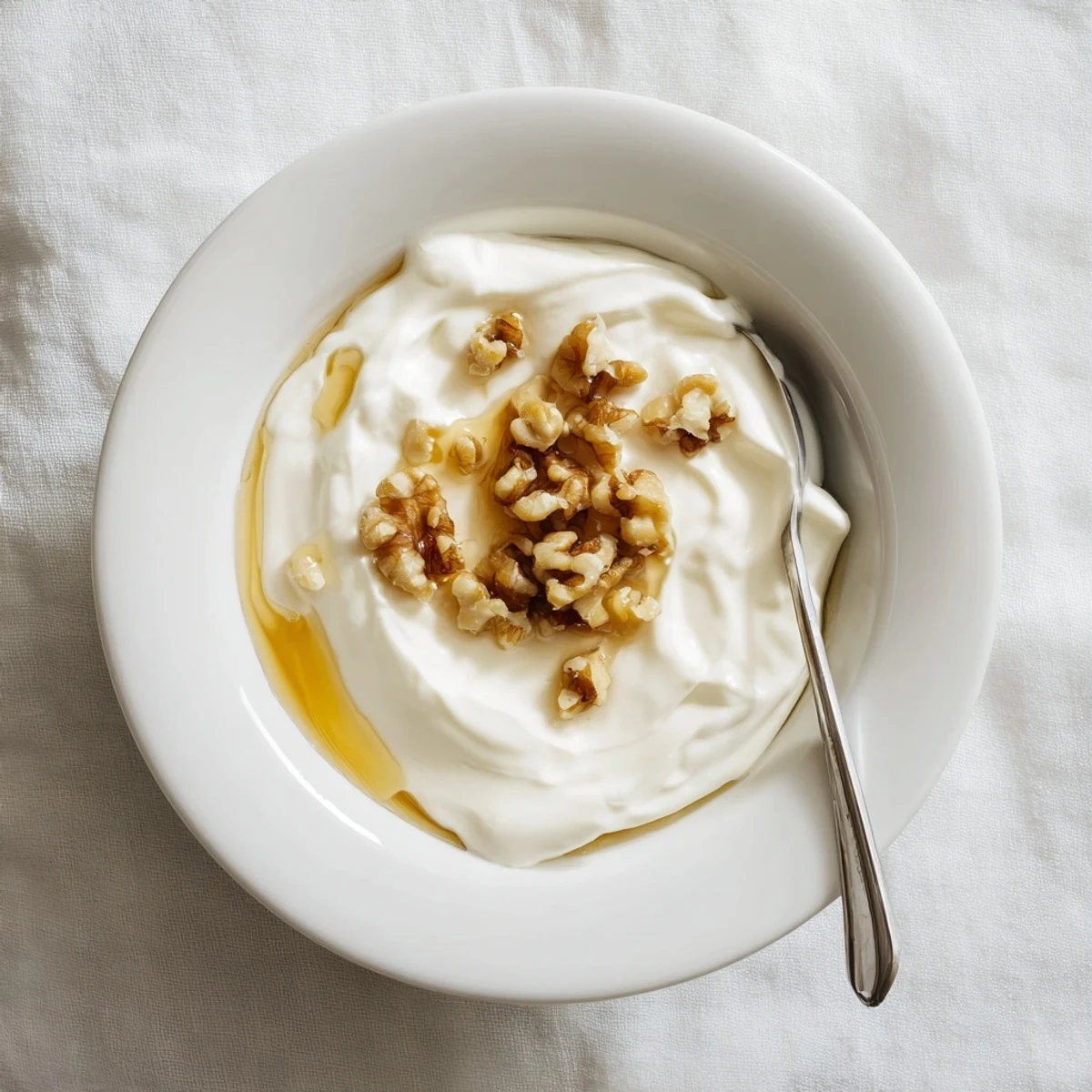 Creamy homemade Greek yogurt in a white bowl topped with fresh honey and walnuts