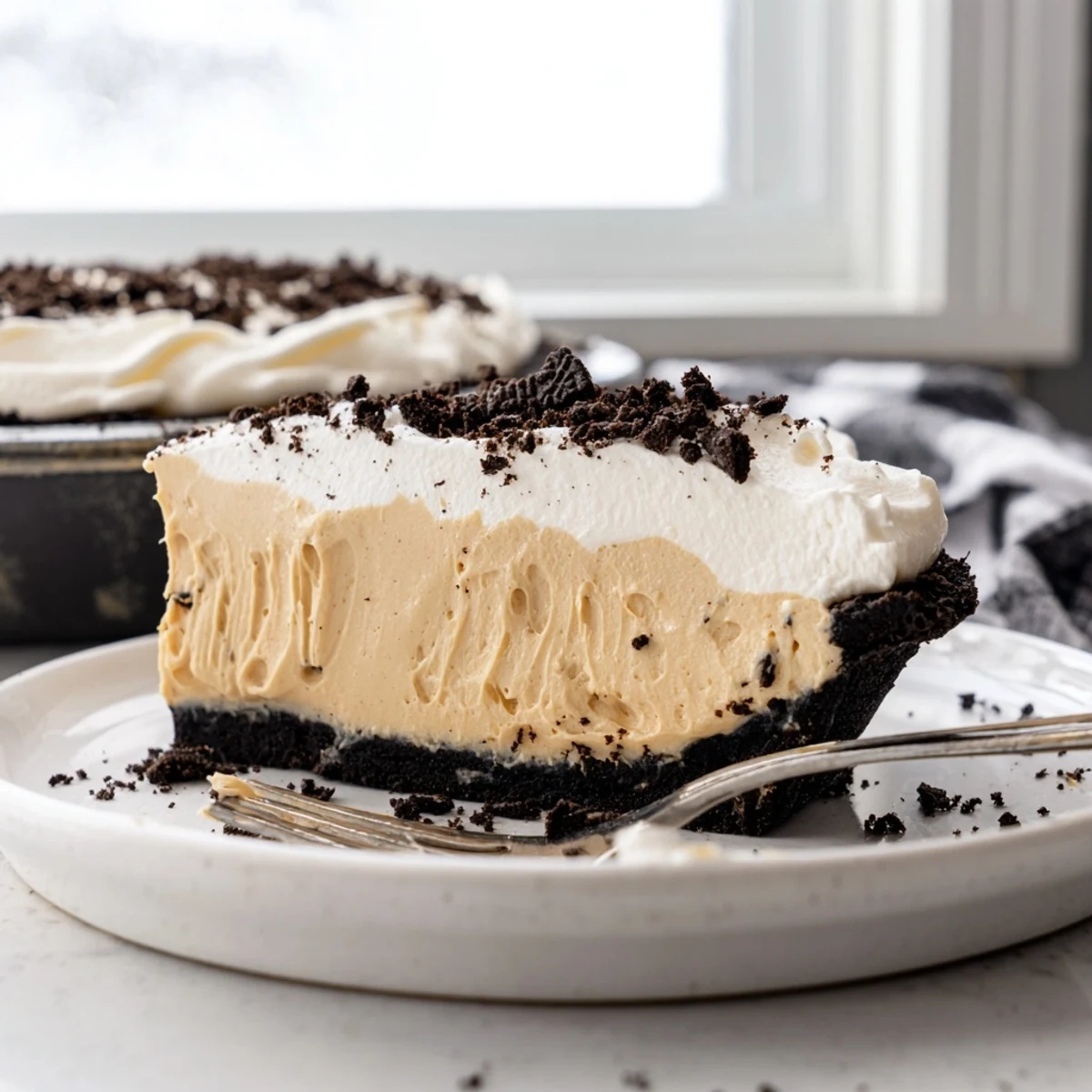 Creamy peanut butter Oreo pie with whipped topping and cookie crumbles on a chilled dessert plate