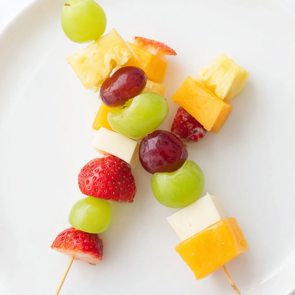 Colorful fruit and cheese kabobs arranged on a rustic wooden serving platter for parties