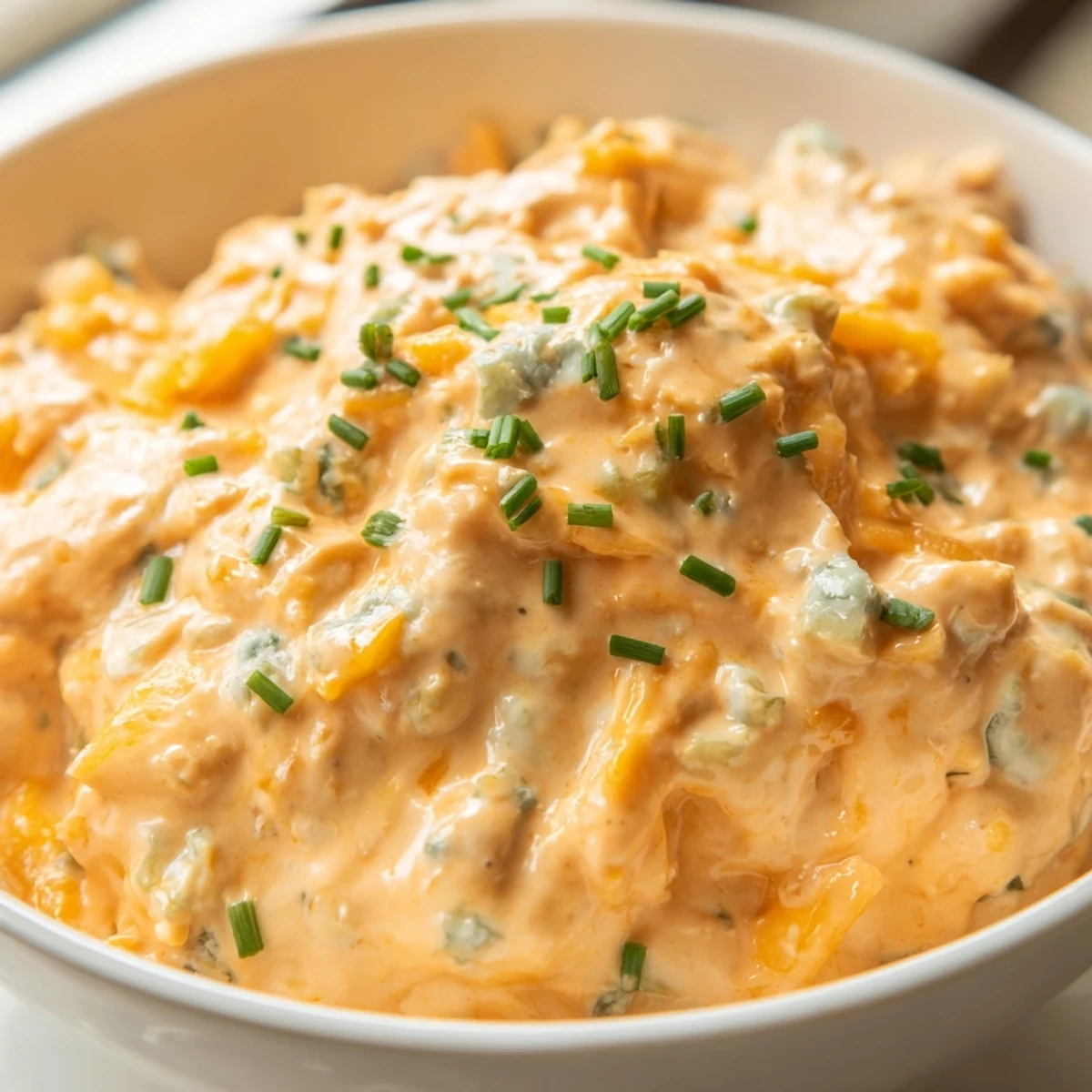 Creamy buffalo pickle dip in a serving bowl surrounded by crunchy chips and fresh veggie sticks for dipping