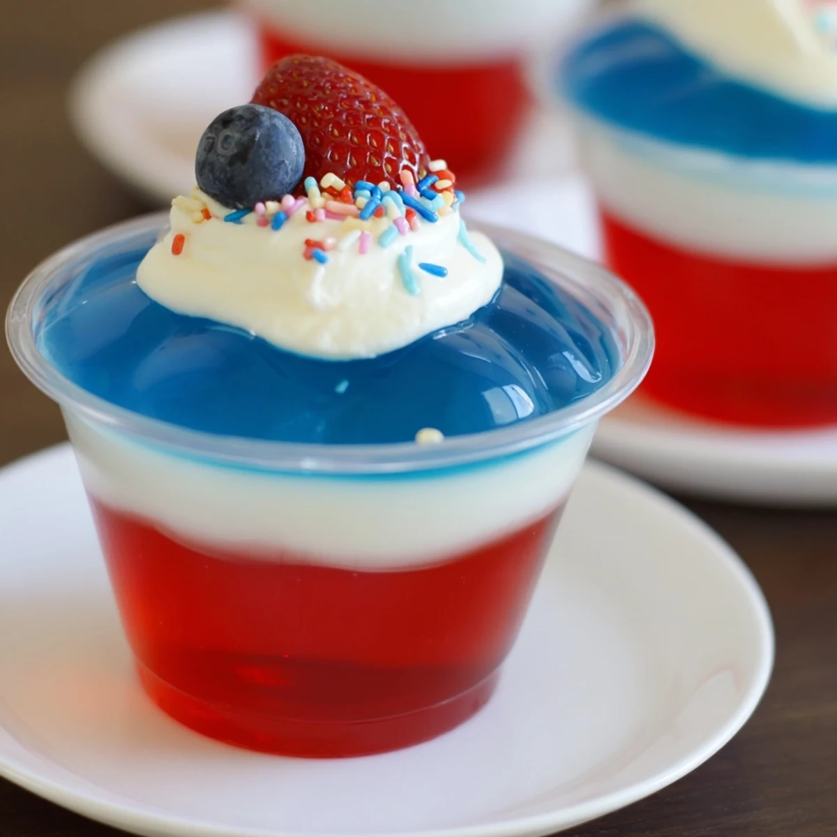 Chilled Red White And Blue Jello Cups with creamy middle layer and berries.