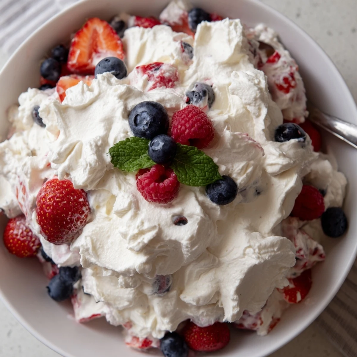 Party-ready Red White Blue Cheesecake Salad served in glasses, fluffy cream, fresh berries