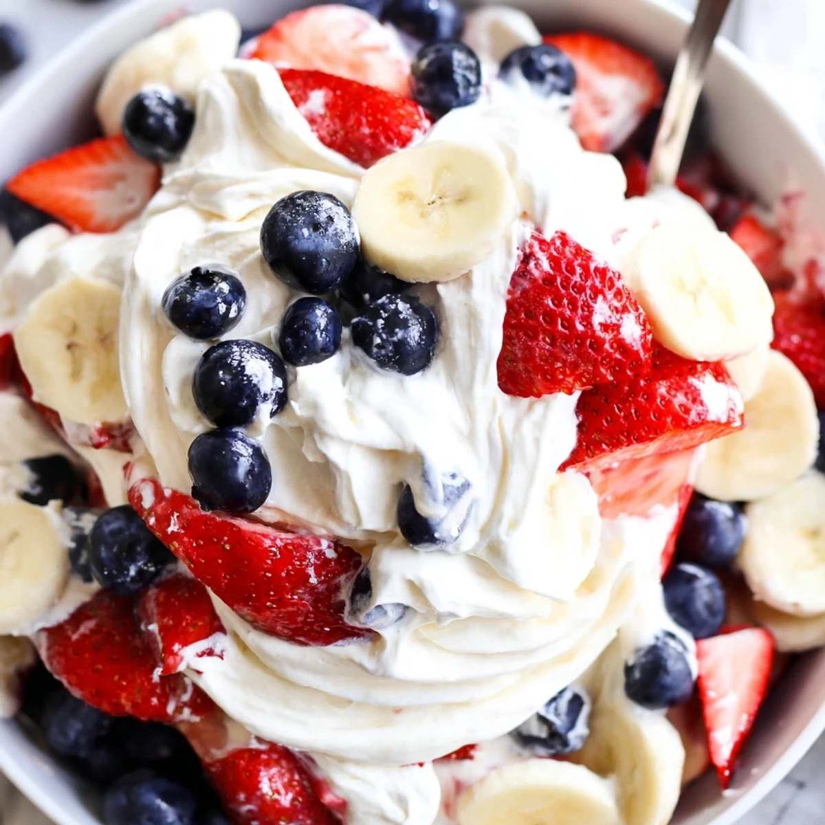 A spoonful of Red White And Blue Cheesecake Salad shows creamy, fruity layers.