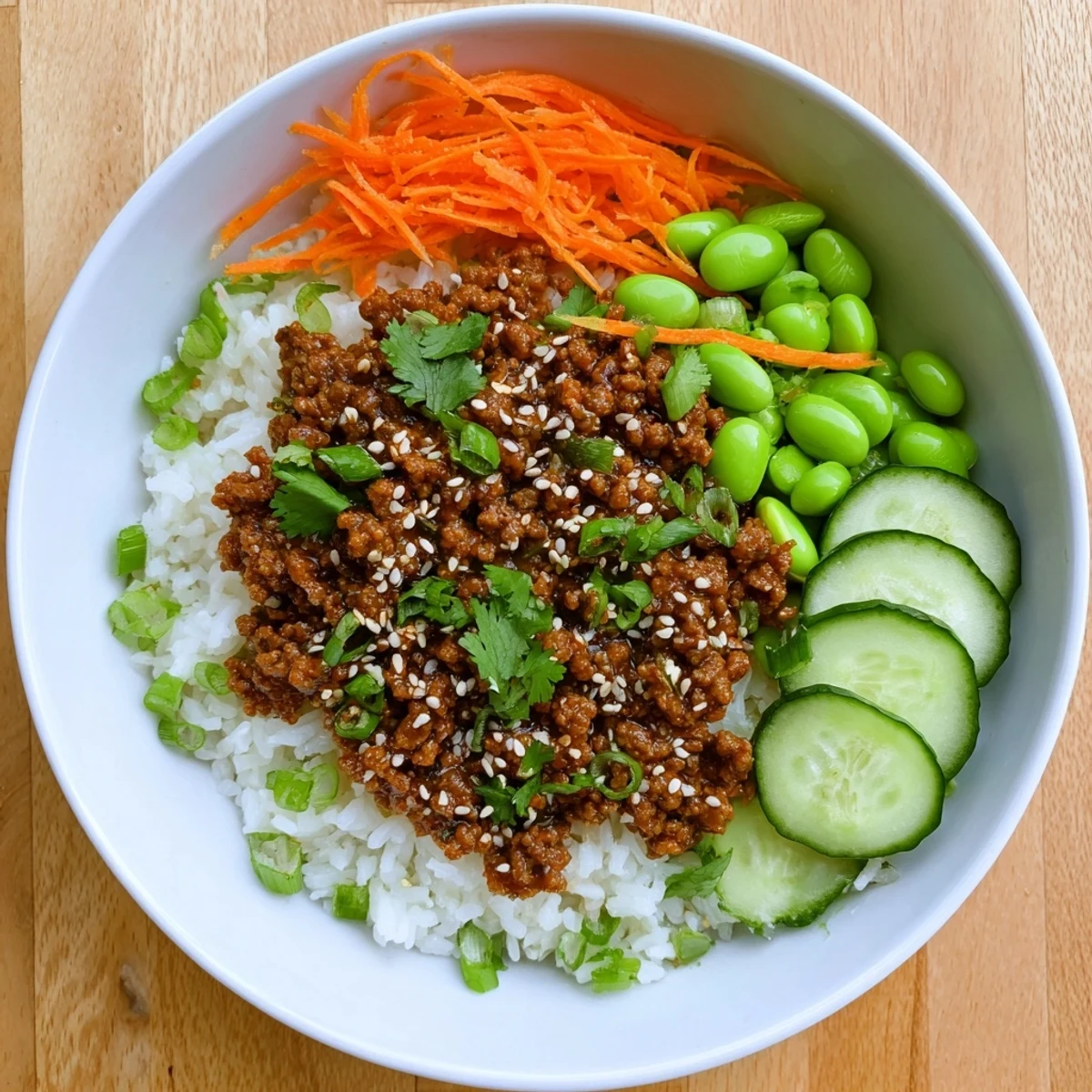 Savory ground beef hot honey bowl served over fluffy white rice with colorful shredded carrots, crisp cucumber slices, and fresh green scallions.