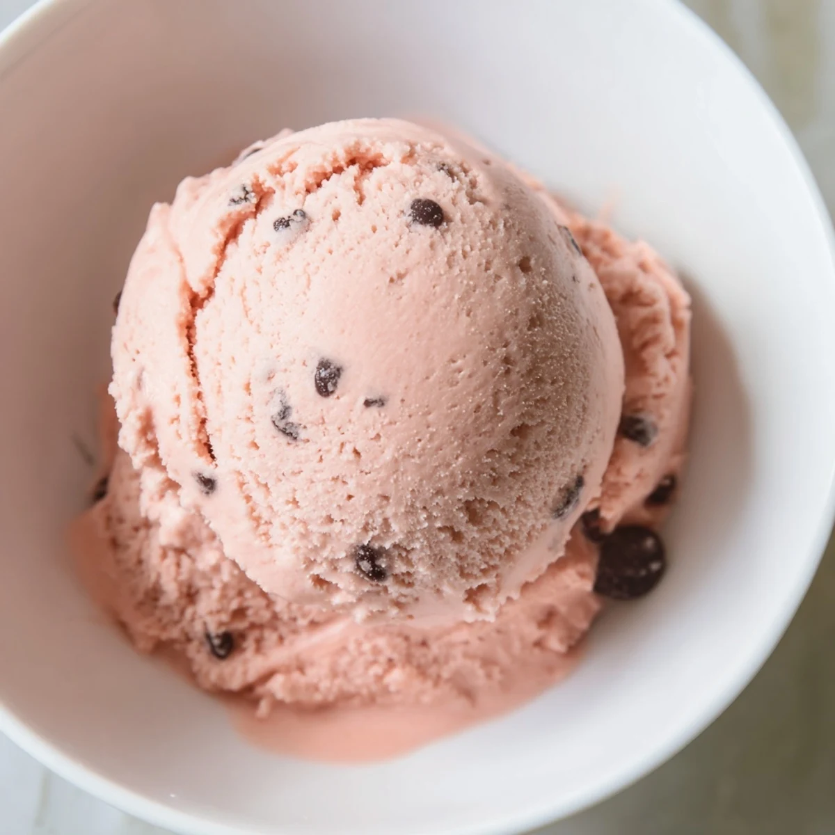 Homemade watermelon ice cream scooped into vintage bowls with fresh watermelon wedges on side