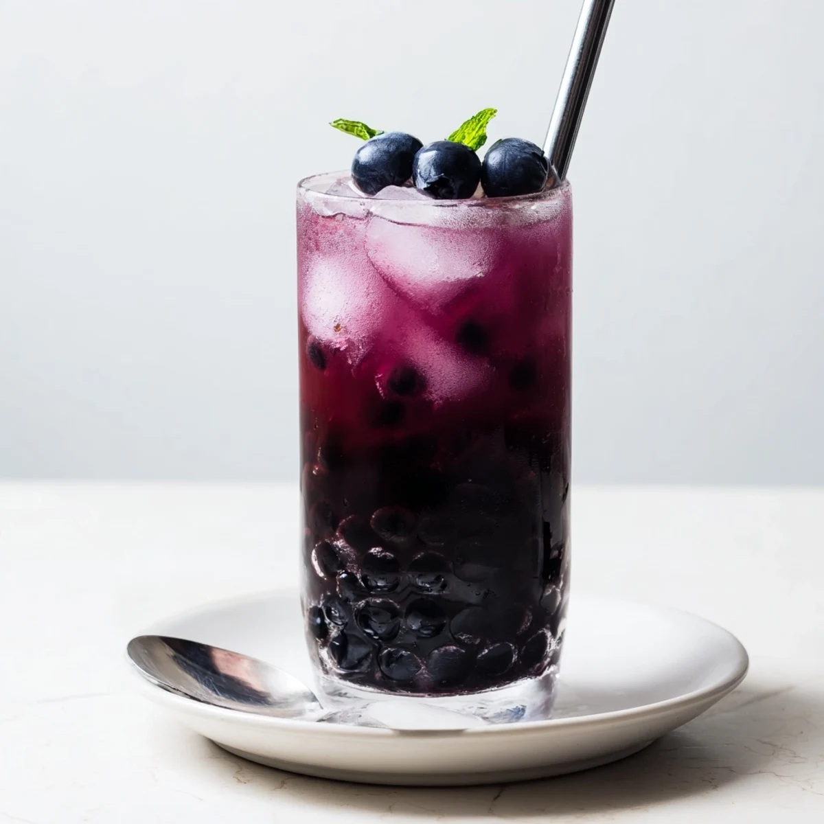 Iced Blueberry Milk Tea Cooler topped with mint sprig, chewy boba, straw